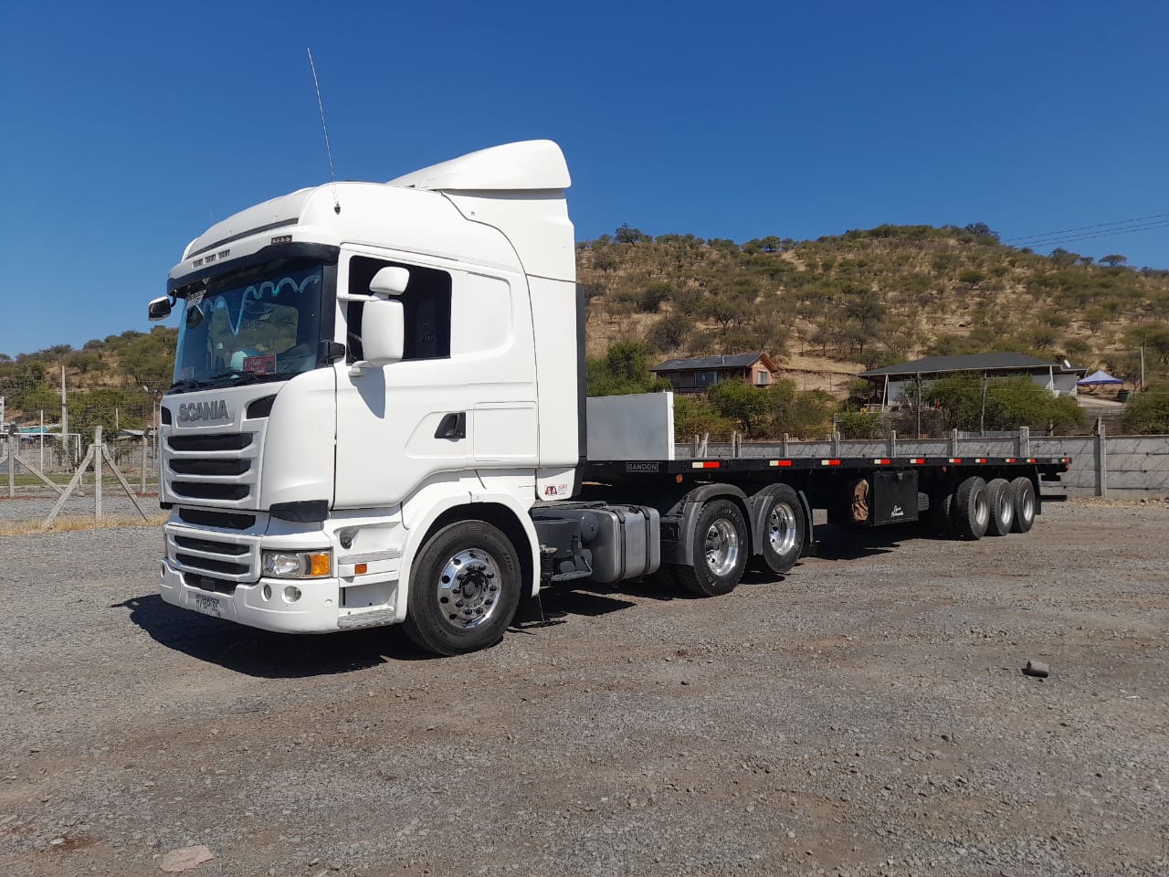 Camión Scania blanco de T Y F Transportes con semirremolque plano en patio de operaciones